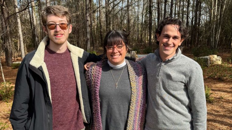 Three young adults standing outside posing together in front of trees