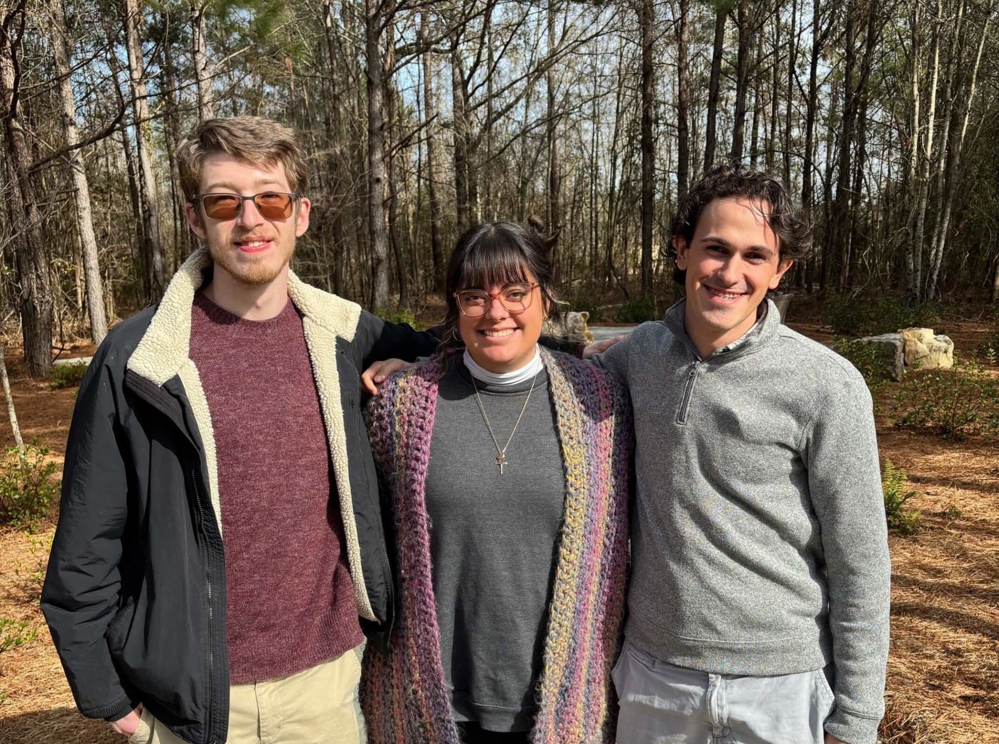 Heritage interns Three young adults standing outside posing together in front of trees