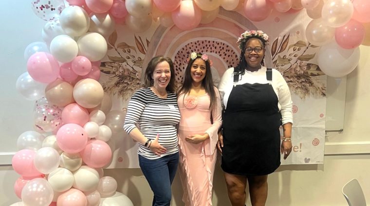 Three expecting mothers posing in front of balloons at a baby shower event