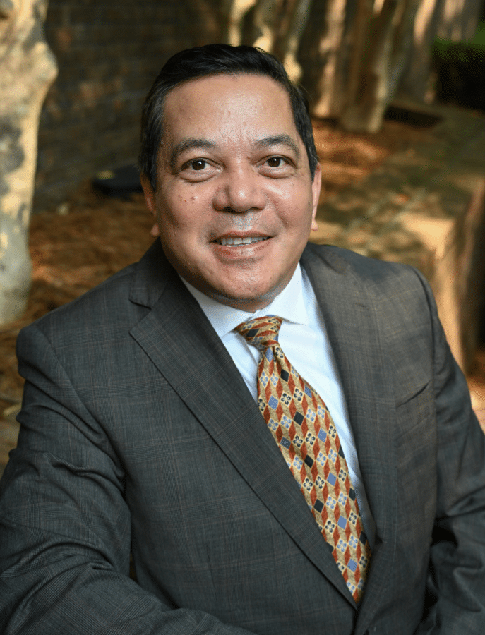Deacon Rick Medina man in a suit posing in front of elevated landscaping