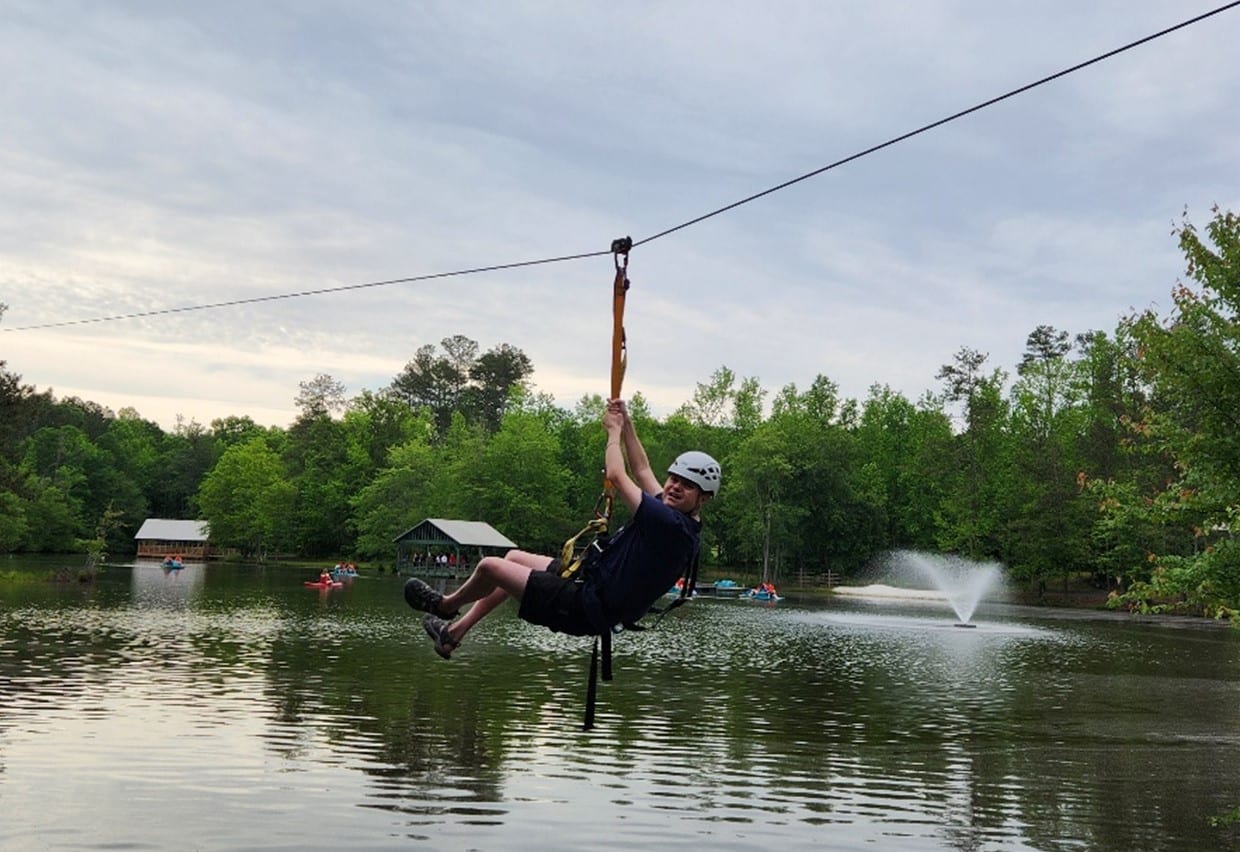 a man ziplining over a body of water surrounded by trees