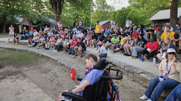 A large group of people sit outside on auditorium-style stone stairs