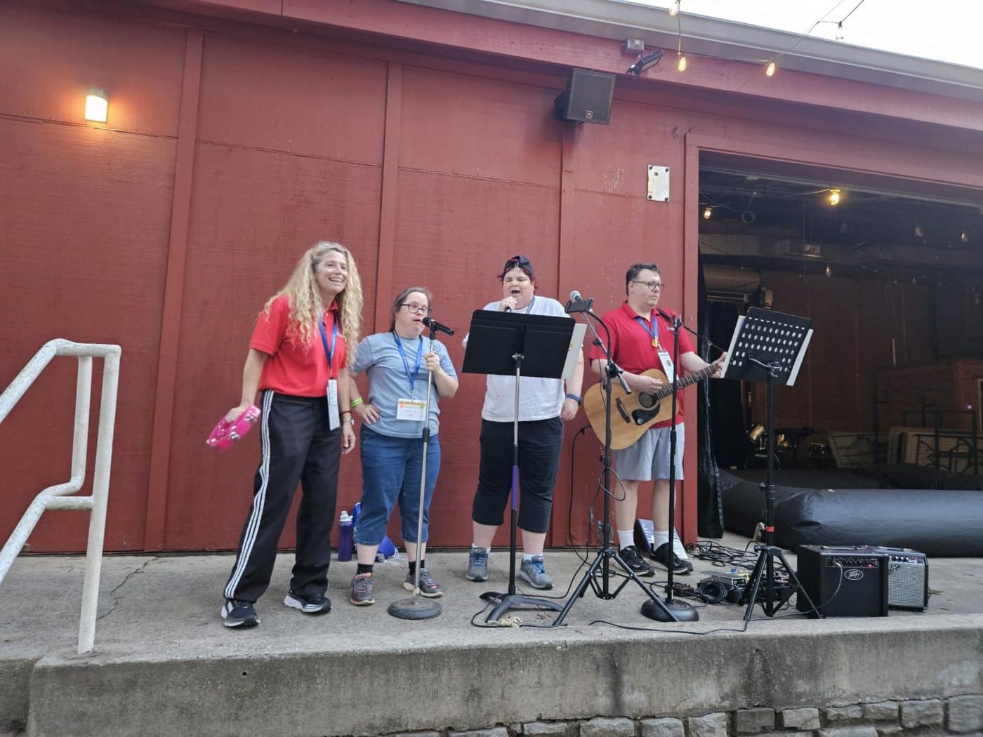 4 people perform on an outdoor platform surrounded by music equipment