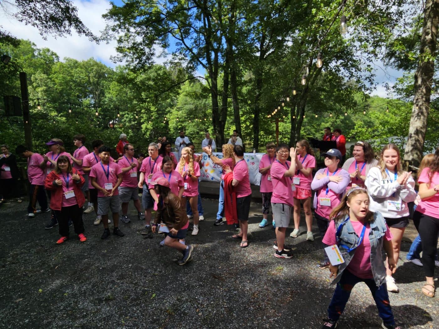 20 youth in matching shirts standing or dancing outside in nature