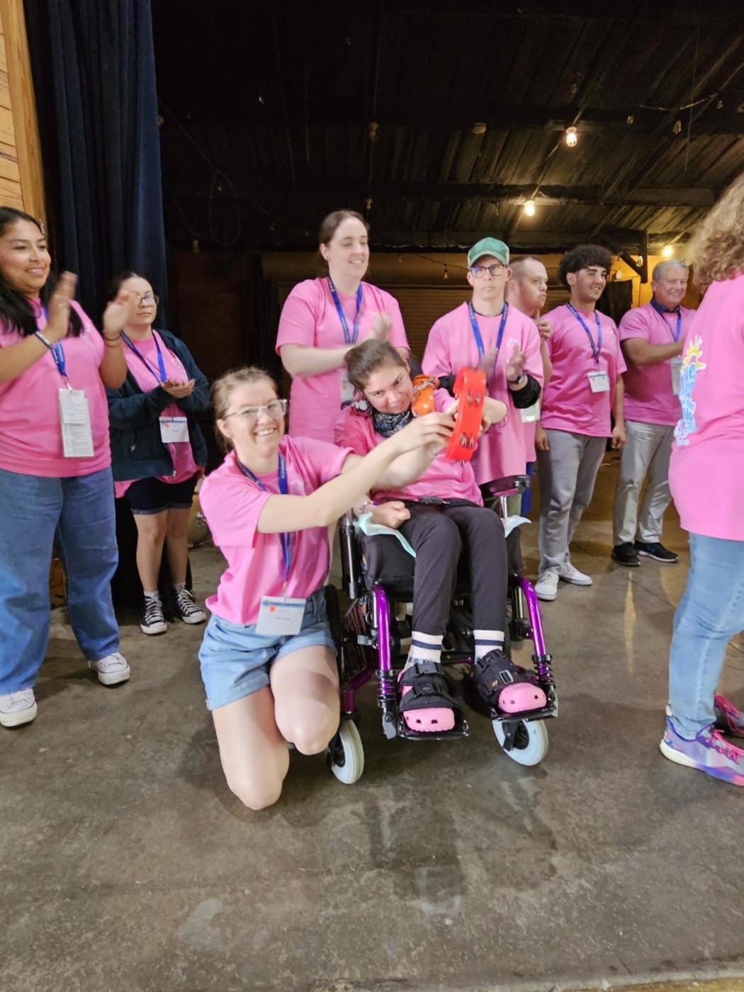 Woman kneels next to someone in a wheelchair, helping them show an item in their hands