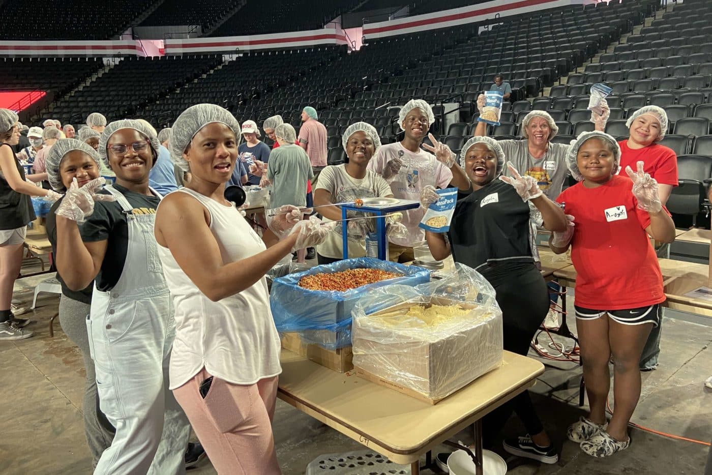 A group of people stop working to smile and pose for the camera, holding food packages.