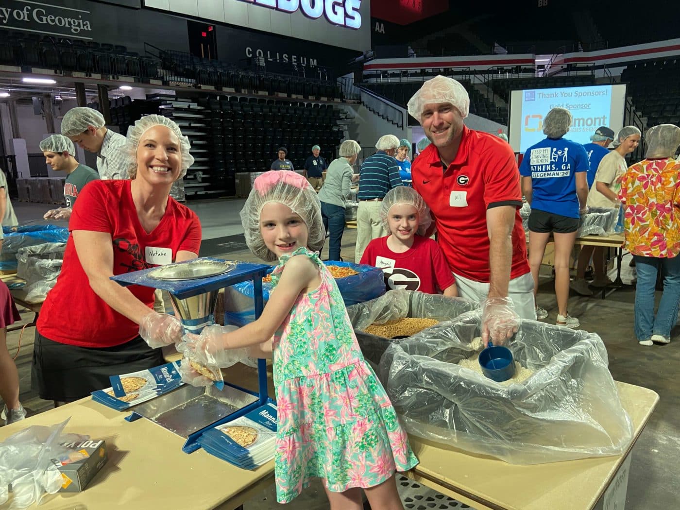 A family pauses while packing meals at a table to smile for the camera