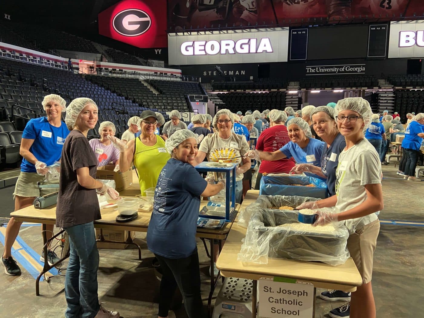 A group of people stop working to smile for the camera, their hands frozen in the middle of packing meals.