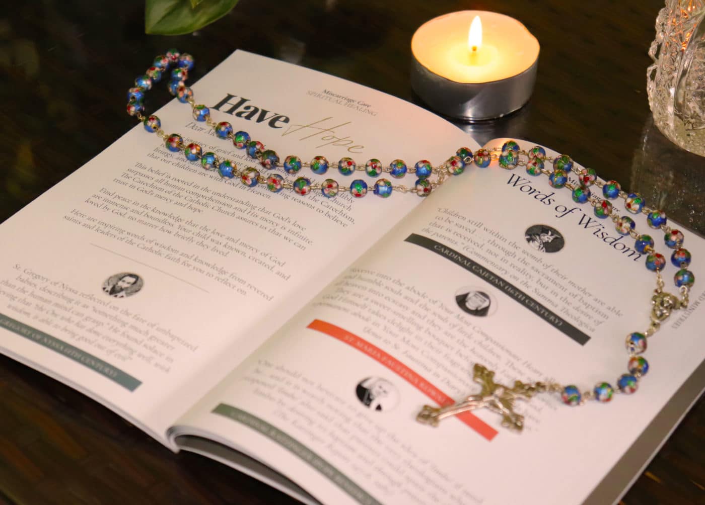 A rosary is placed on an open book with a lit candle close by