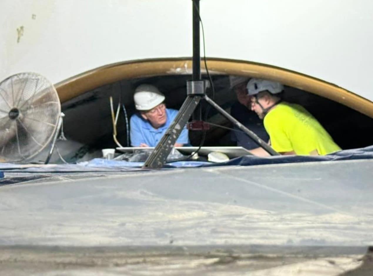 Men in hard hats crouch under a narrow site