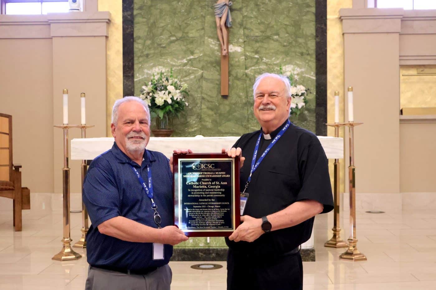 Two men holding a plaque award with the altar of a Catholic in the background