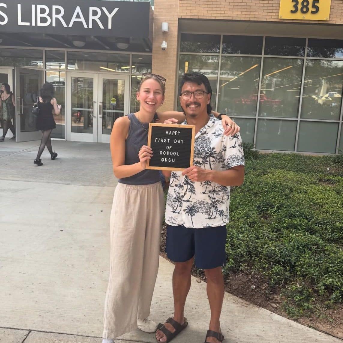 Two young adults pose in front of a school library
