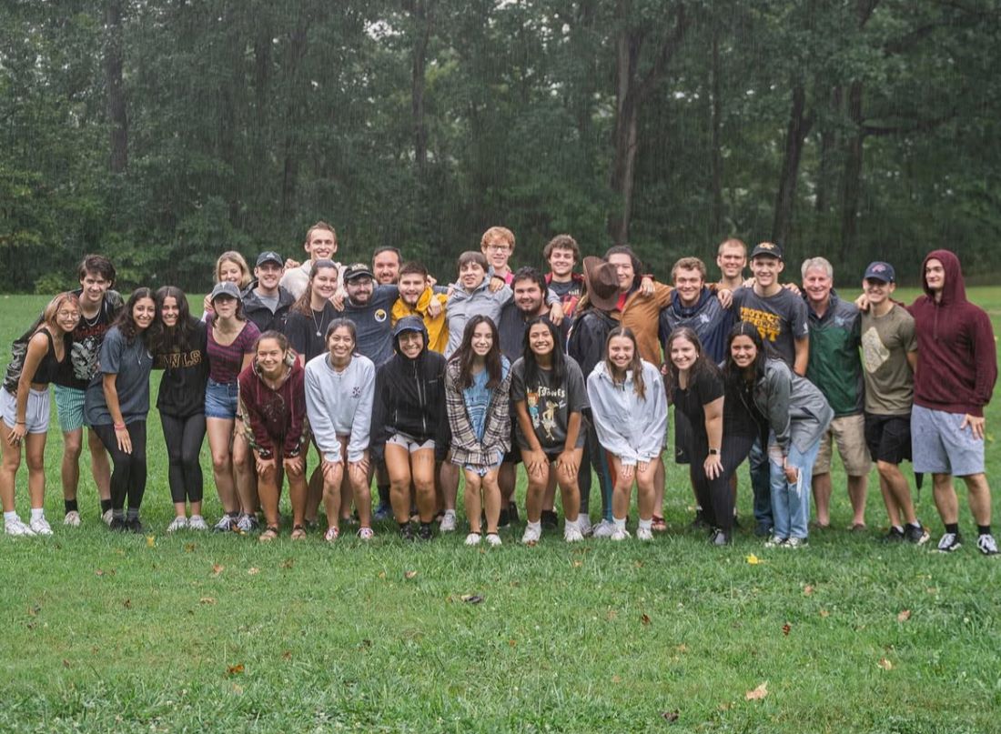 Large group of students and one priest pose on a field in the rain