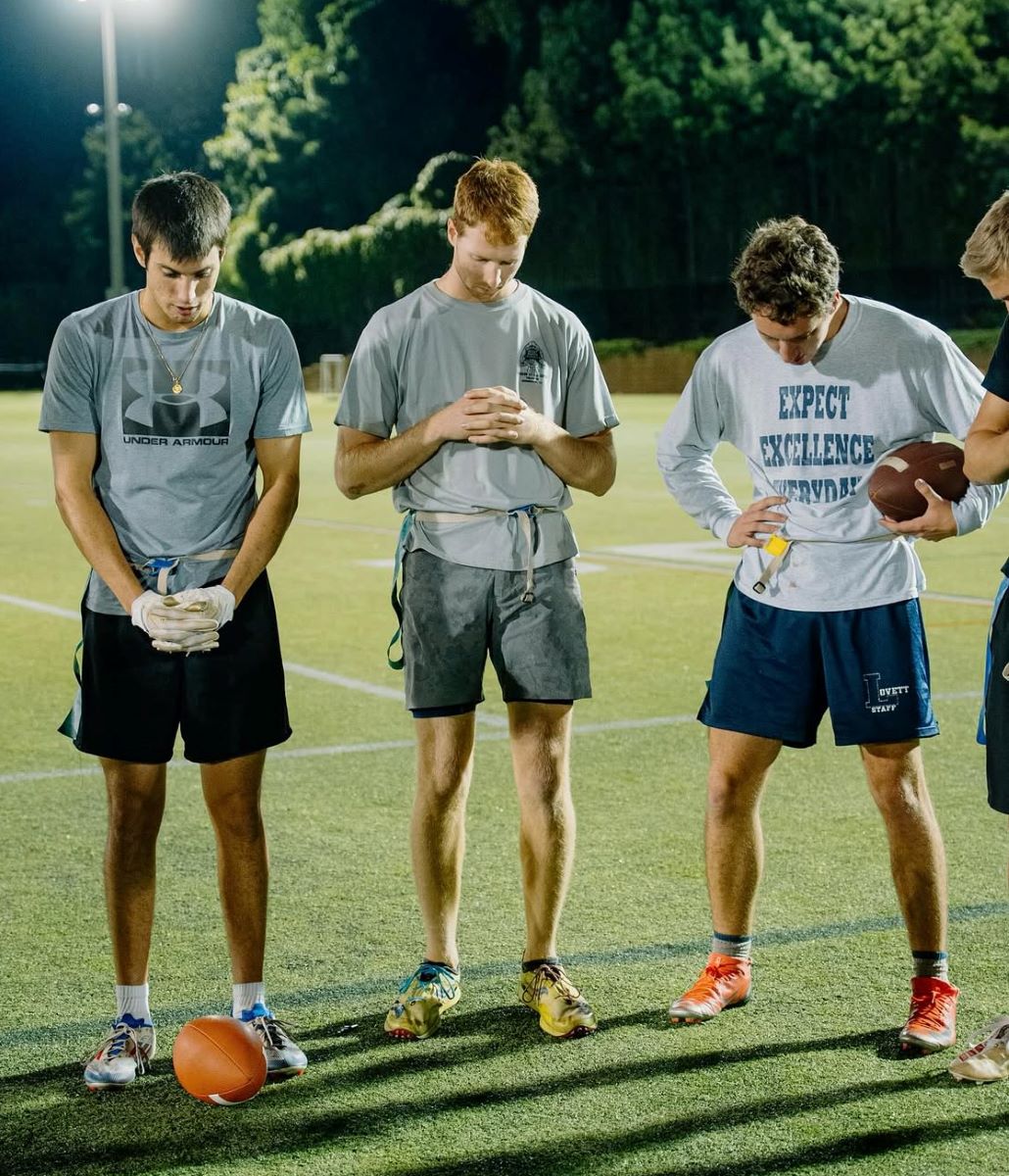 3 students pray on a field