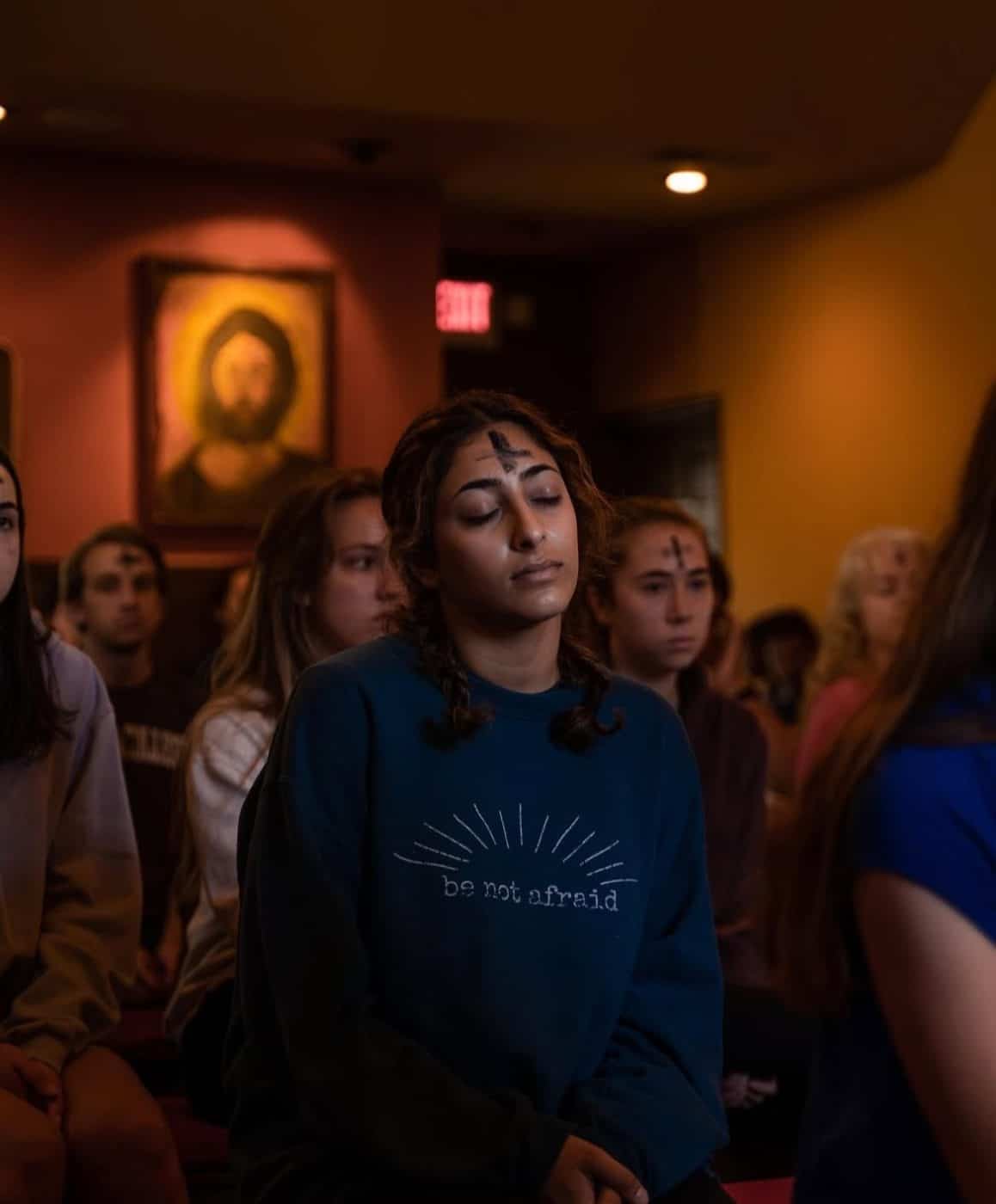 students sit at a church service with an ash cross on their foreheads