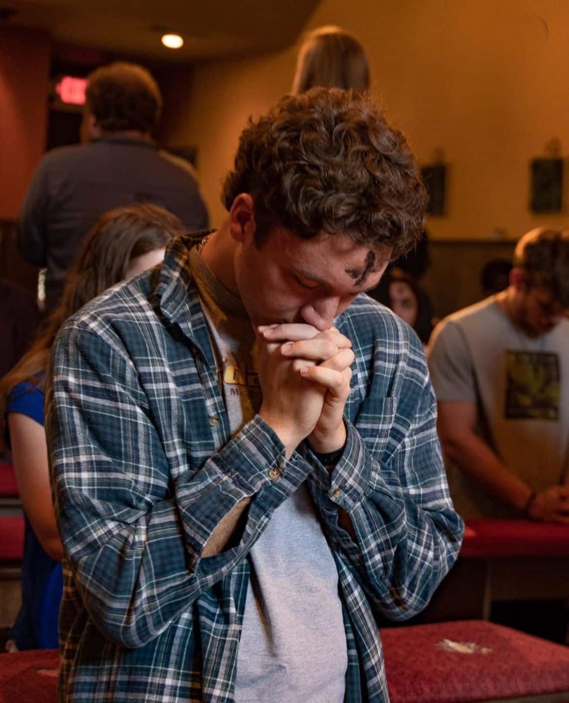 A student kneels with his head down and hands crossed in prayer