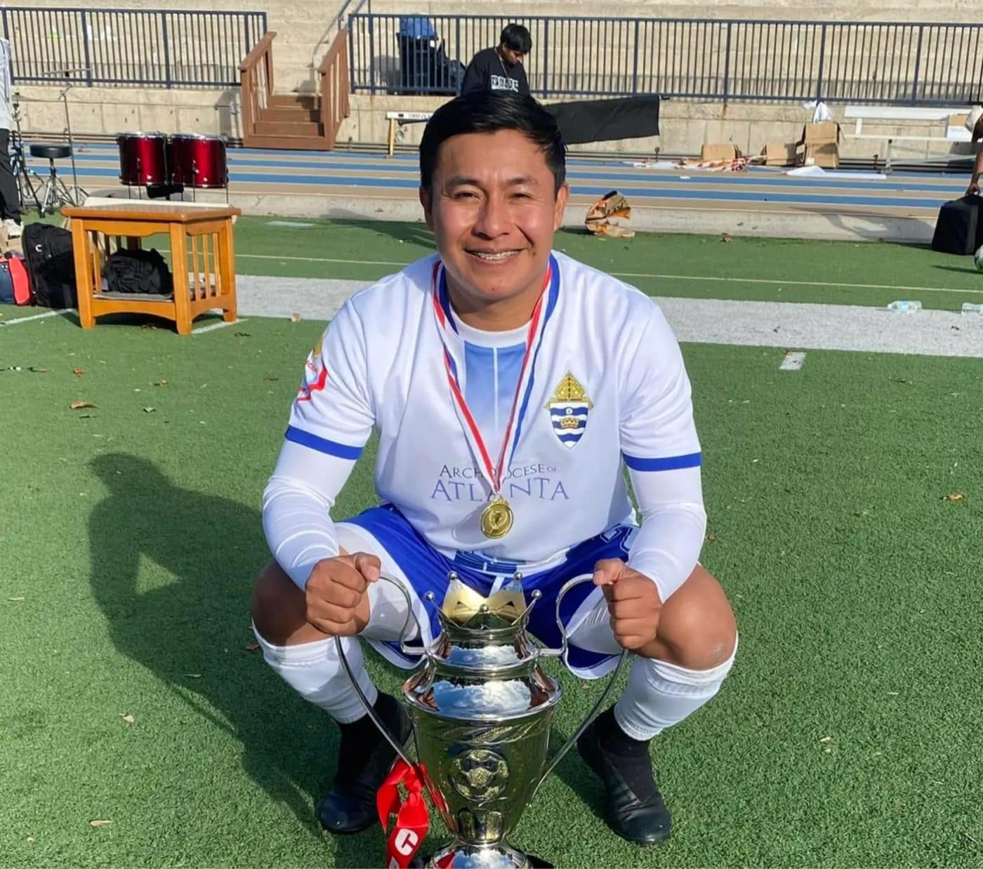 Man poses with a trophy on a soccer field