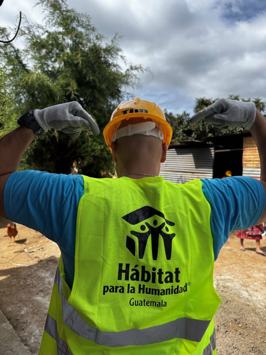 A person in a construction hat and vest points toward a Habitat para la Humanidad Guatemala logo on his vest