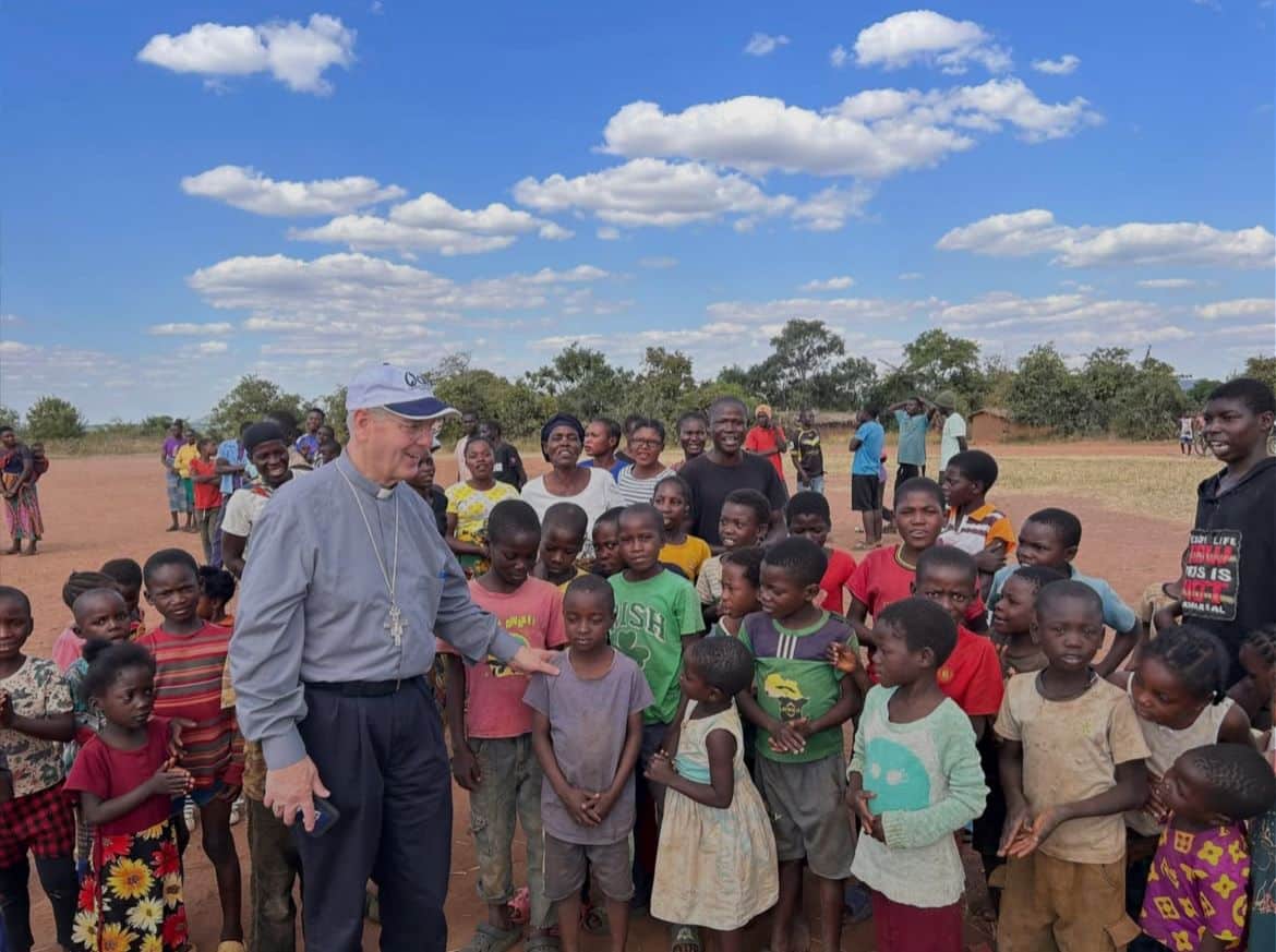 Archbishop Hartmayer interacts with many children on a field in Zambia