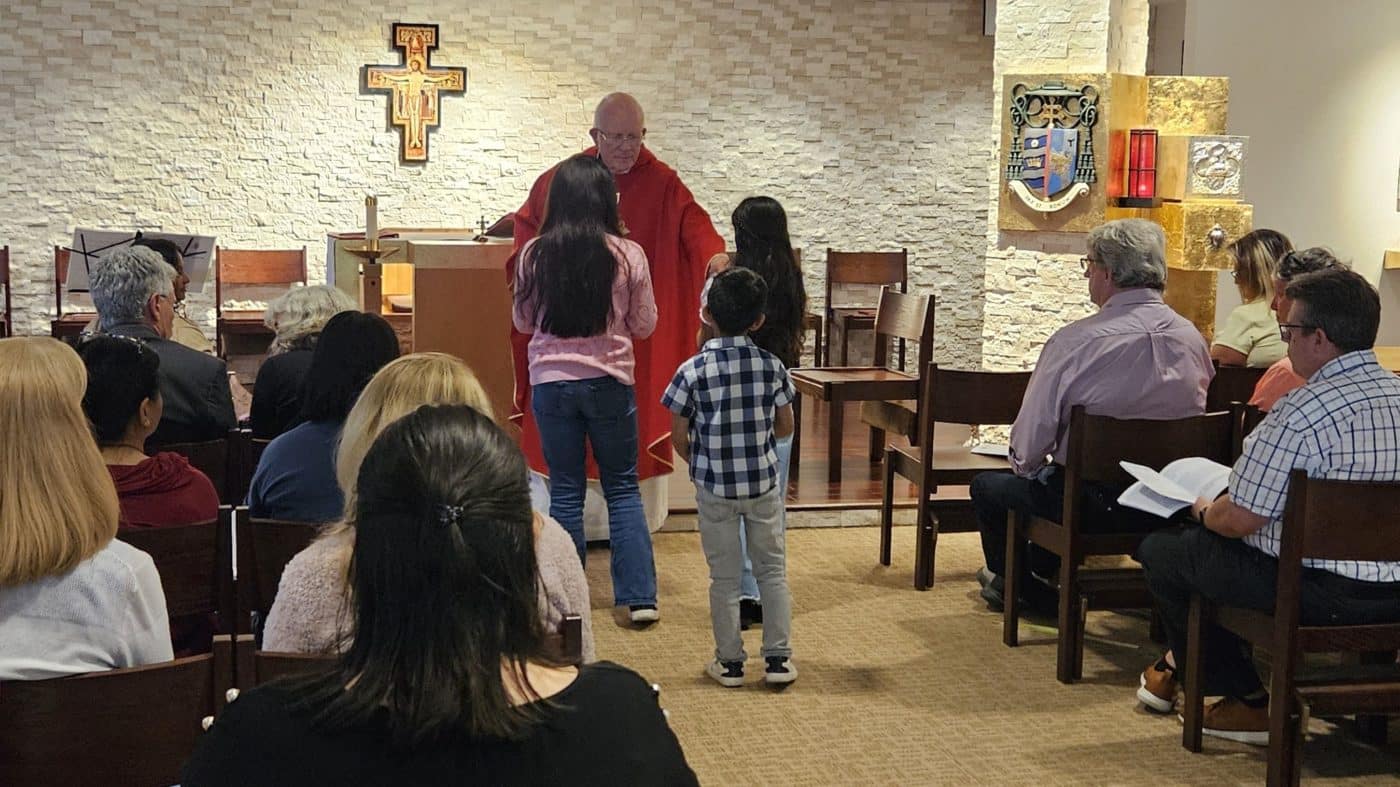 a priest greets children offering gifts at the altar