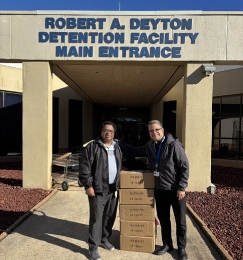 two men stand outside of a building that says Robert A. Deyton Detention Facility Main Entrance