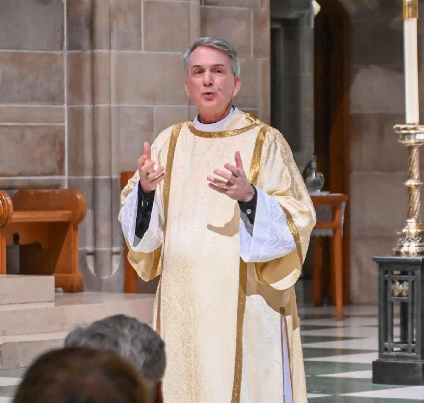 a man in clergy attire speaks at the front of a church to a group