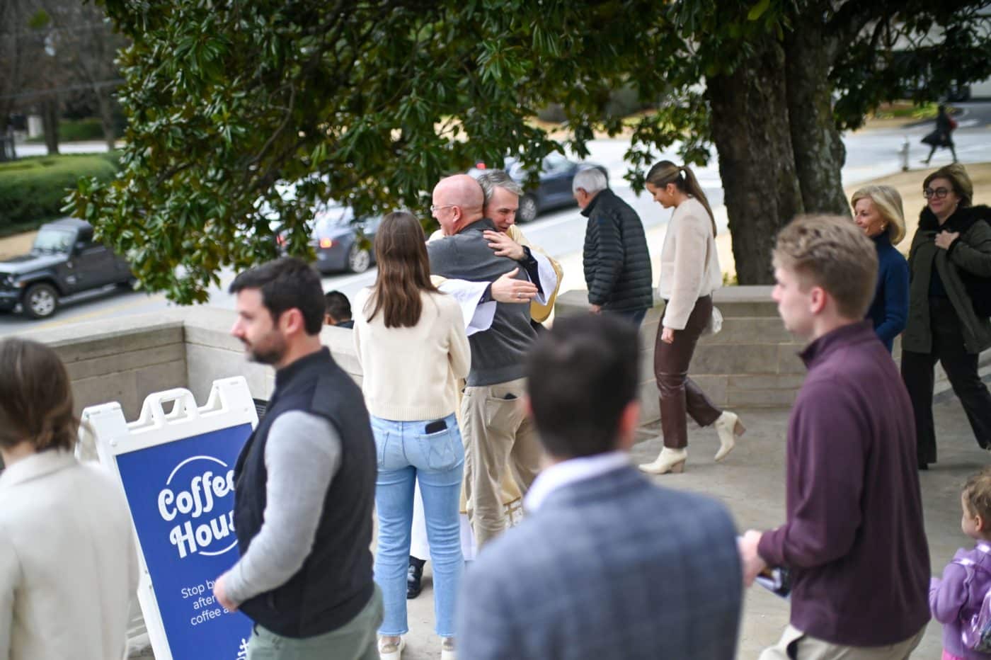 a community of people gather outside, conversing and hugging