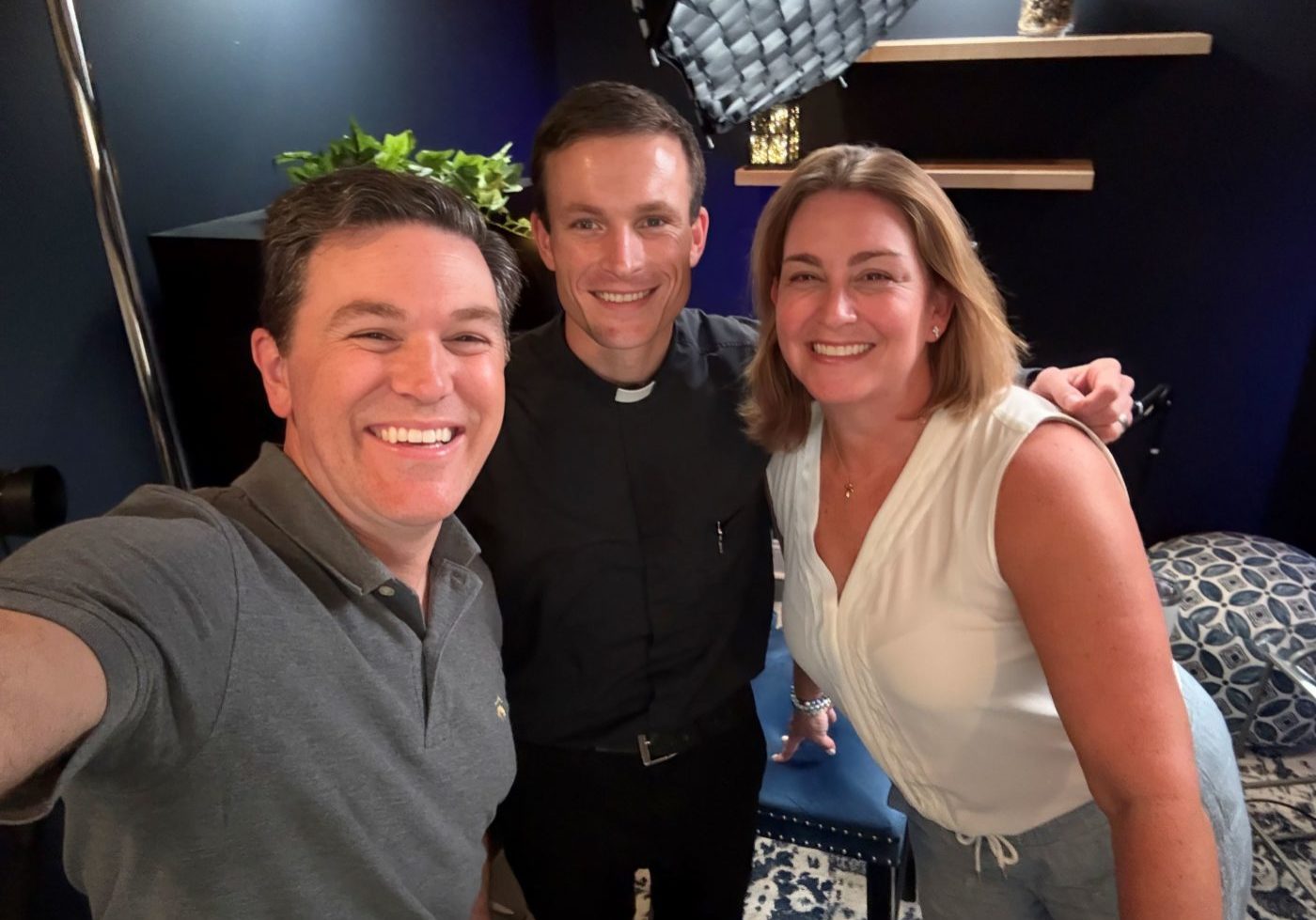 A priest poses with two people in a recording studio