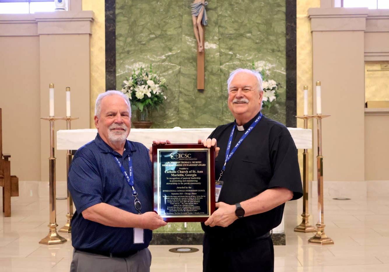 Two men holding a plaque award with the altar of a Catholic in the background
