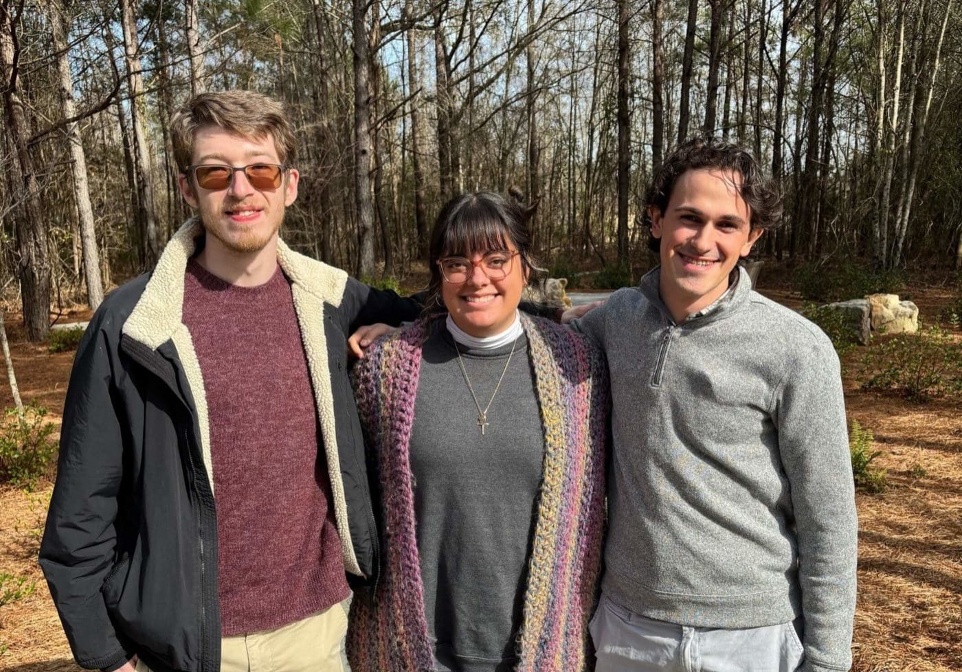 Three young adults standing outside posing together in front of trees