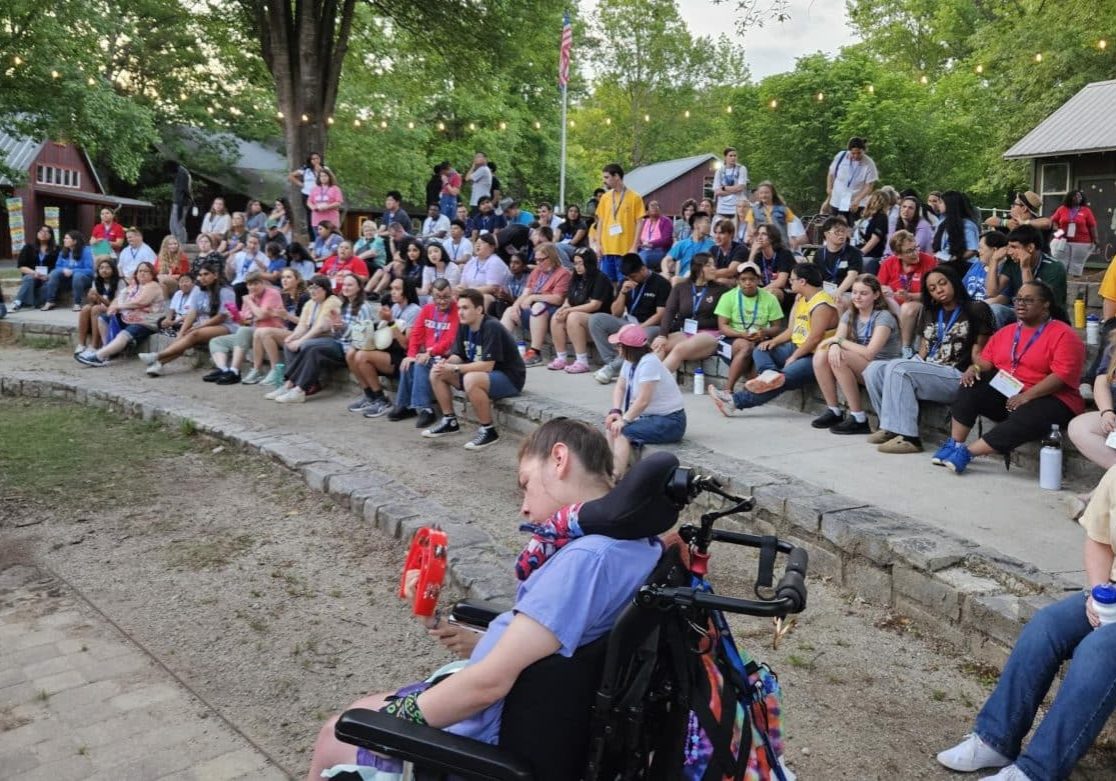 A large group of people sit outside on auditorium-style stone stairs