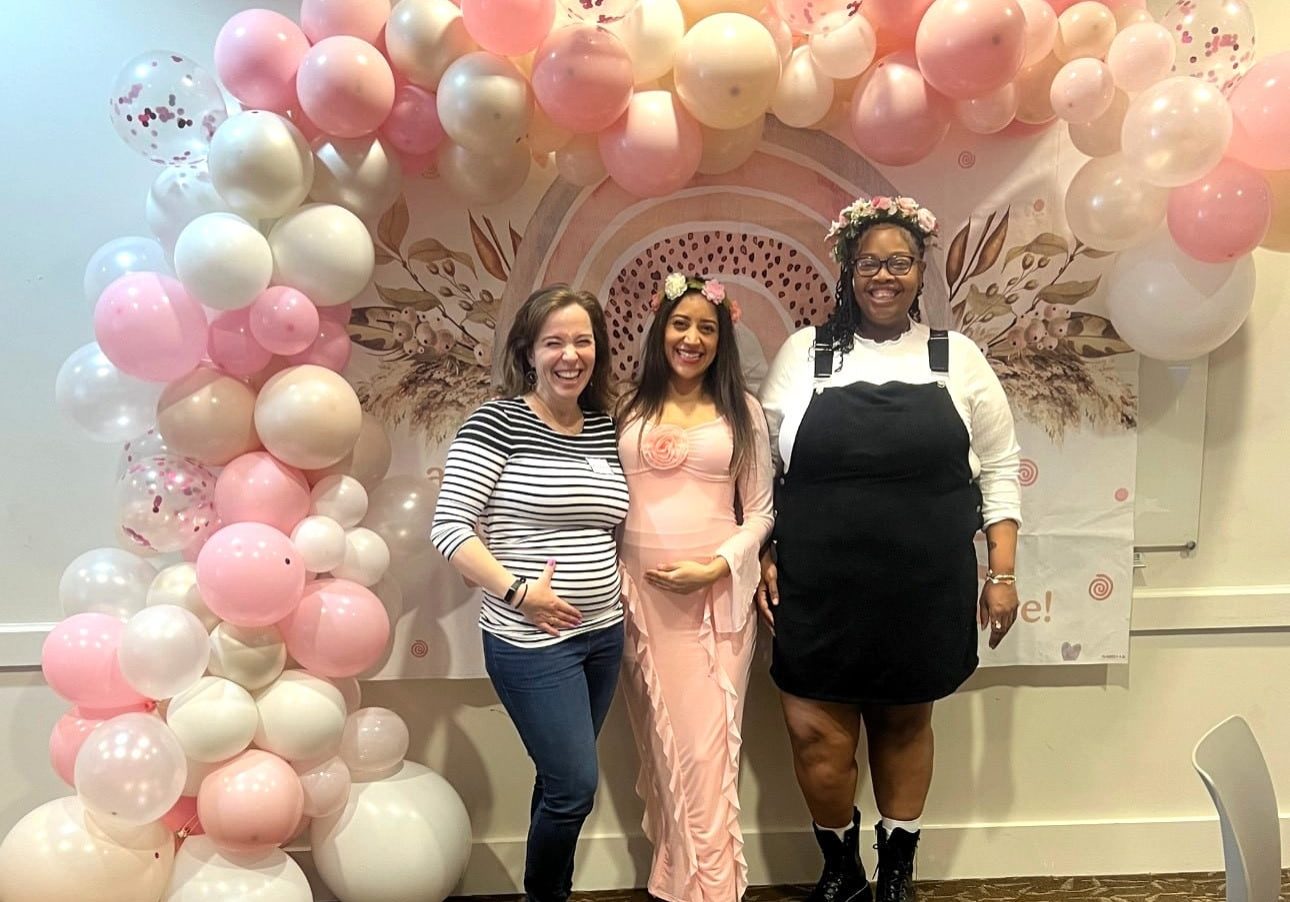 Three expecting mothers posing in front of balloons at a baby shower event
